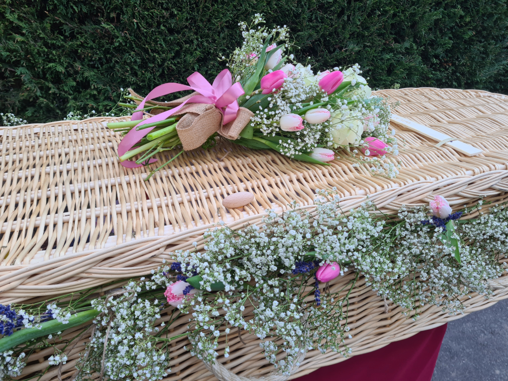 Pink and white flower spray and garland on wicker coffin