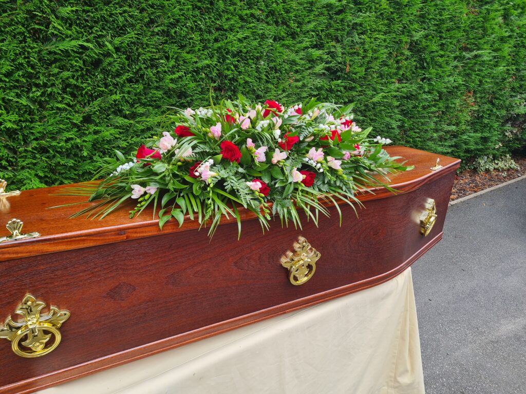 Traditional wooden coffin with handles and traditional funeral flower spray