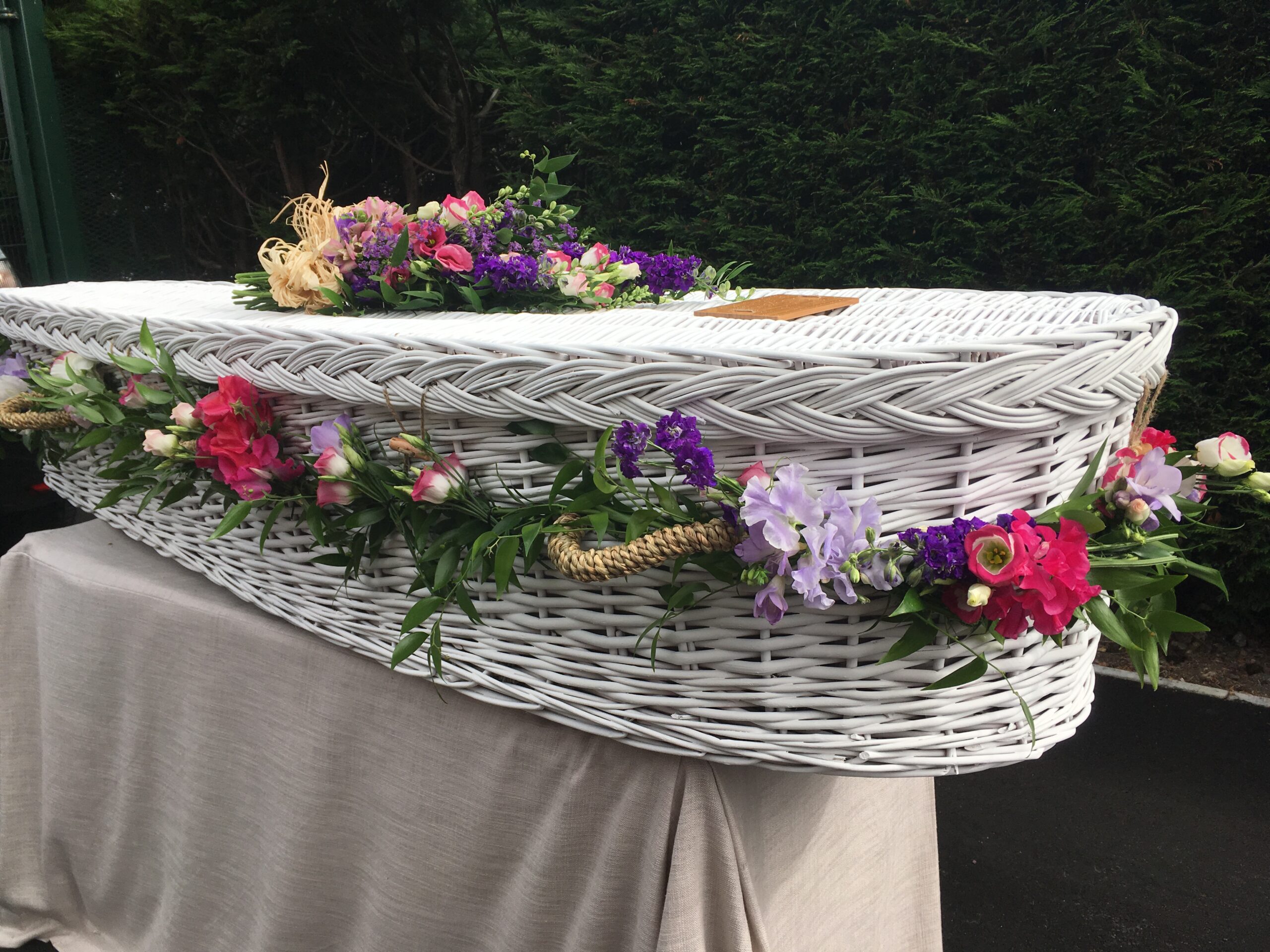 White wicker coffin with colourful funeral flower arrangement and garland